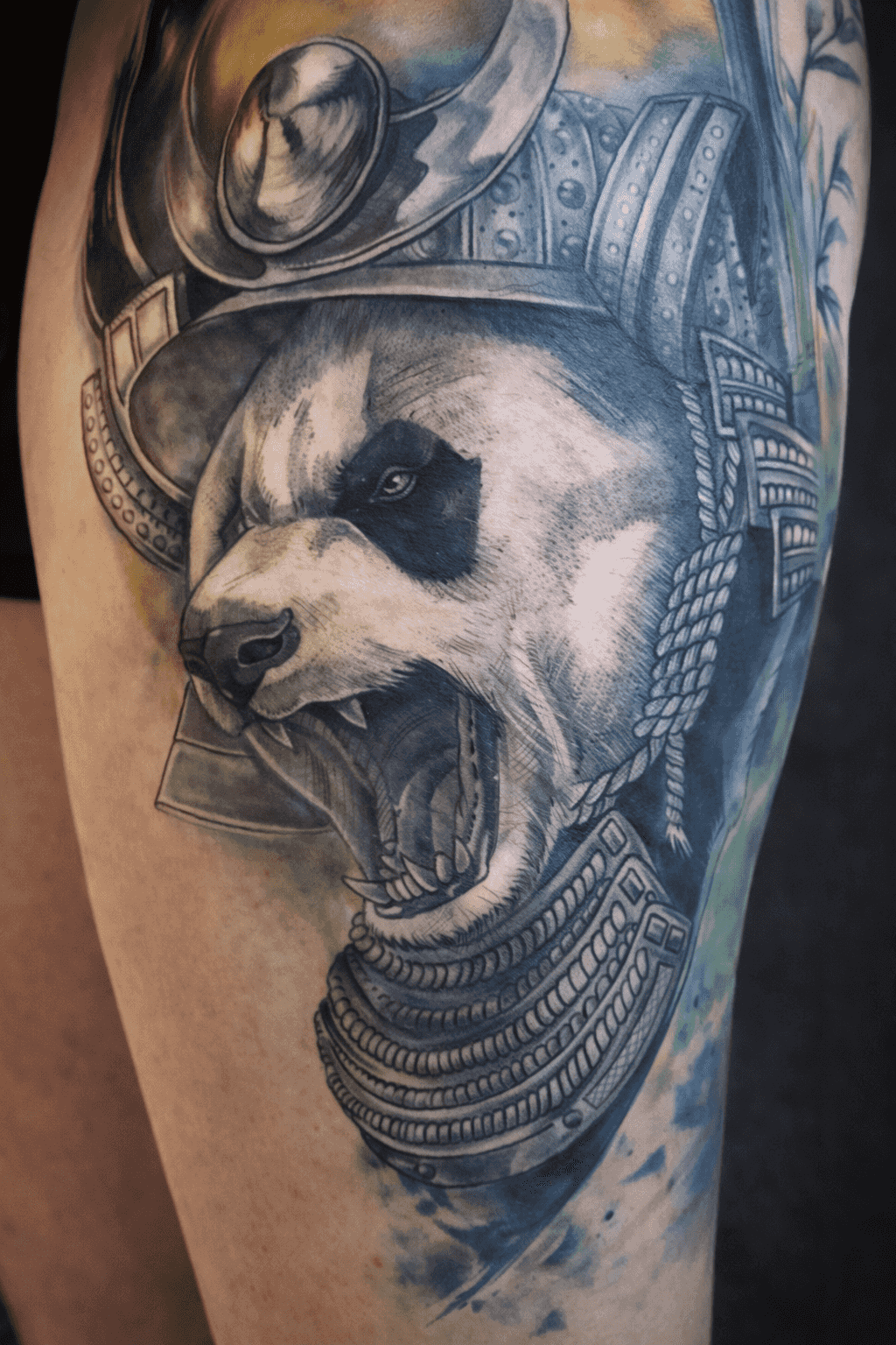 Tatouage d'un panda rugissant en armure de samouraï avec un ombrage détaillé, réalisé par Steven Chaudesaigues au Bastia Tattoo, salon de tatouage à Bastia, avec des accents d'encre verte et bleue.