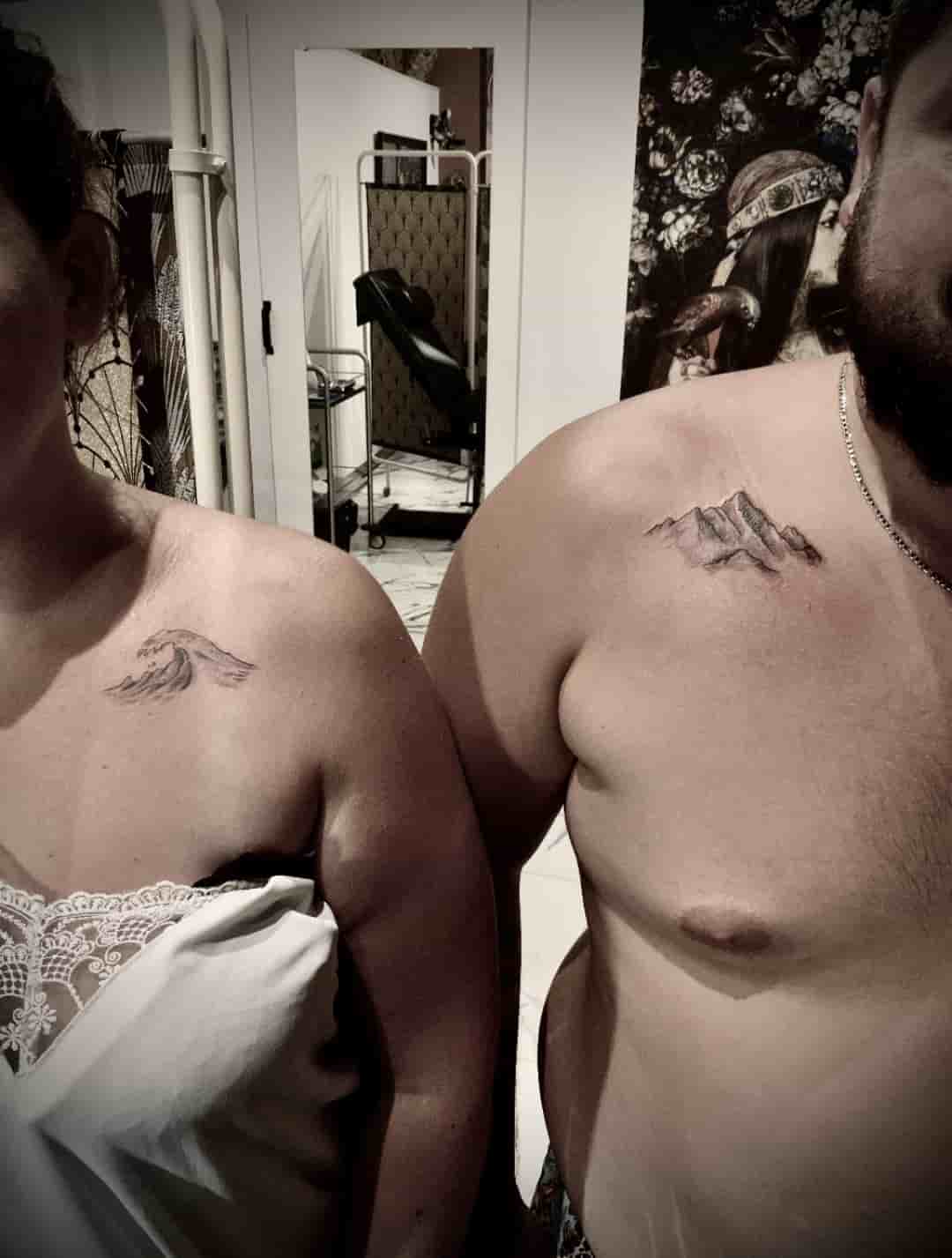 couple avec un tatouage à l'épaule représentant une vague chez la femme et une montagne chez l'homme en noir et gris