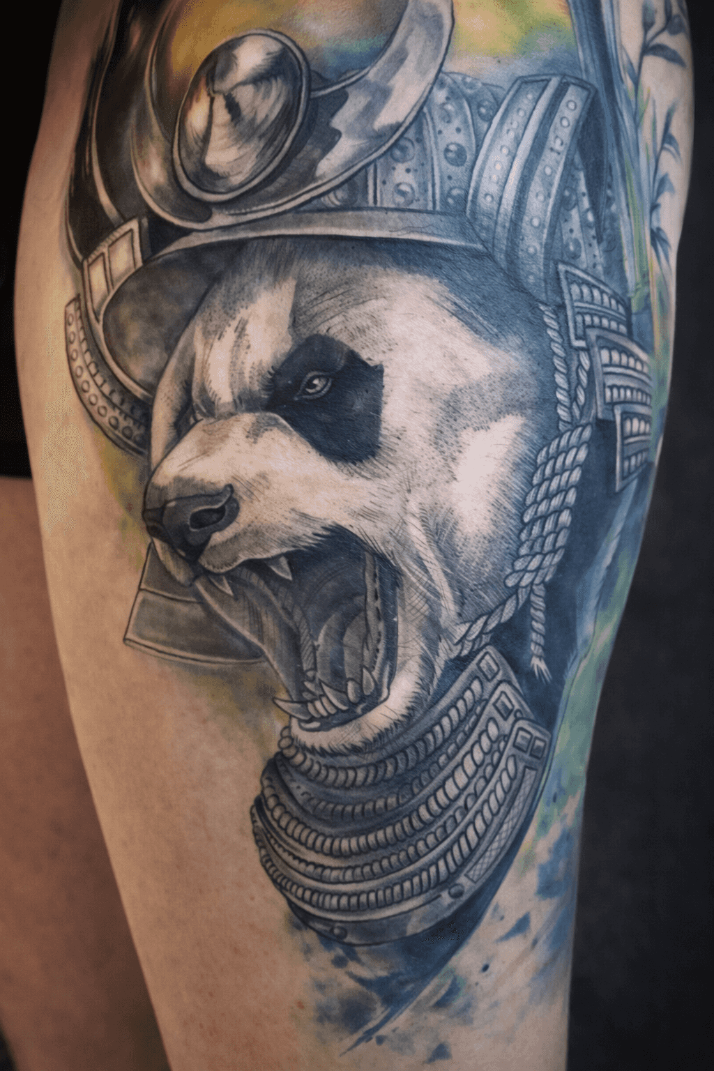 Tatouage d'un panda rugissant en armure de samouraï avec un ombrage détaillé, réalisé par Steven Chaudesaigues au Bastia Tattoo, salon de tatouage à Bastia, avec des accents d'encre verte et bleue.