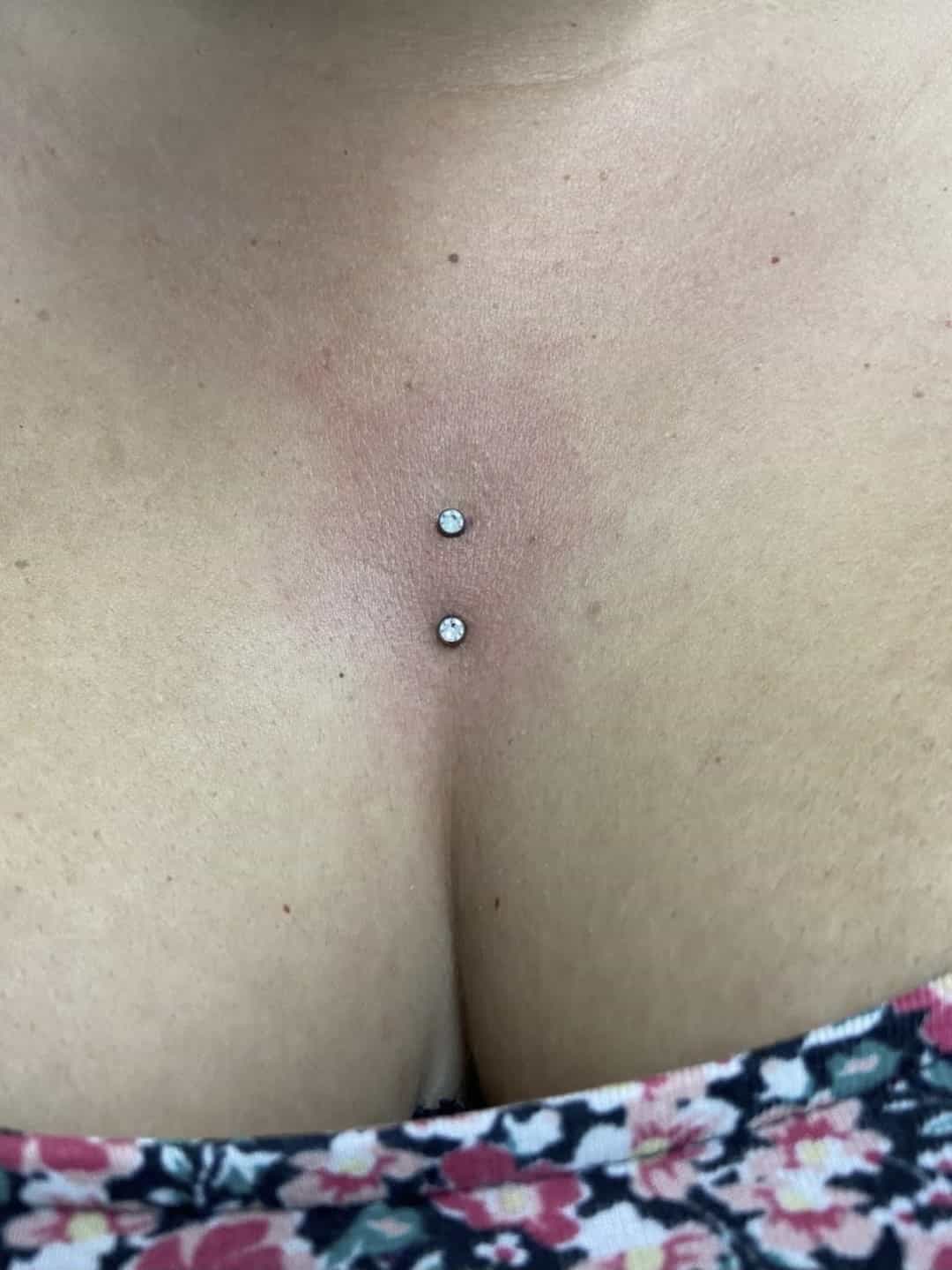 Piercing sur la poitrine avec deux petits clous ronds en diamant au-dessus d'un haut à motifs floraux, réalisés par Nadia au salon de piercing Bastia Tattoo à Bastia.